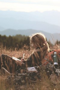 Woman writing in field with mountains